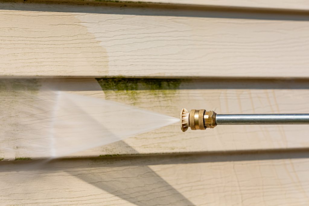 Hose cleaning mold off of vinyl siding on a house.